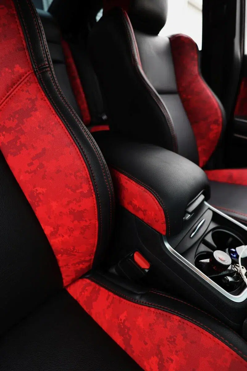Custom car interior featuring red and black digital camo faux leather upholstery on sport seats and armrest.
